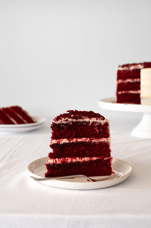 A slice of red Velvet Cake covered in cream cheese icing with red crumb garnish on top 