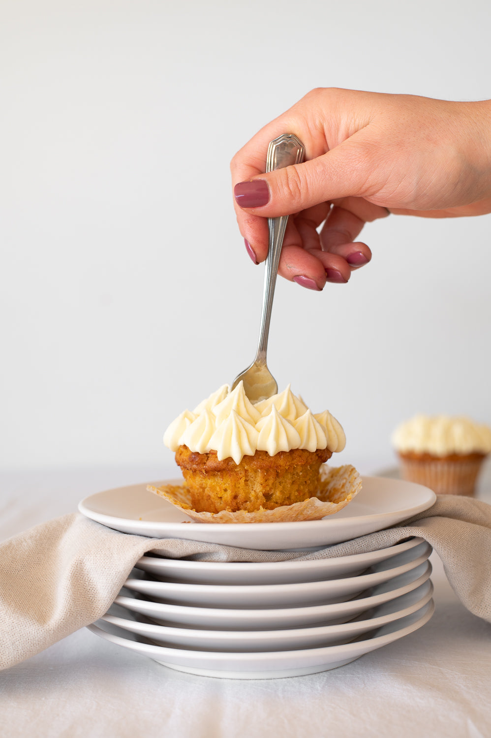 A stack of plates holding a carrot cake cupcake with piped cream cheese icing 