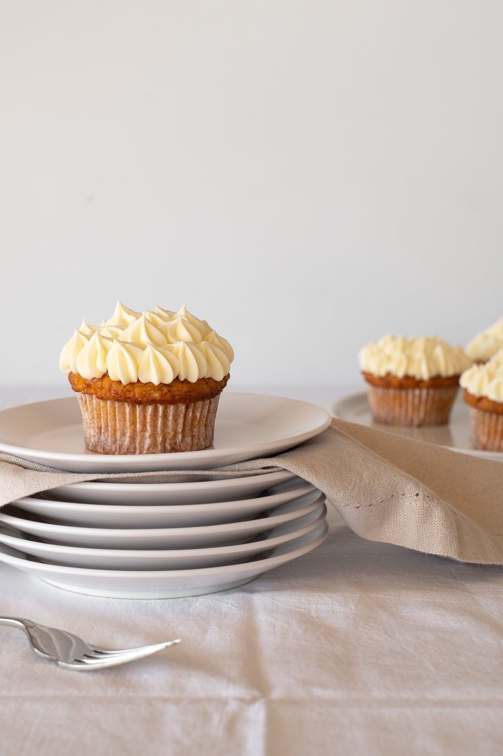A stack of plates holding a carrot cake cupcake with piped cream cheese icing 