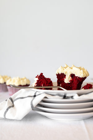 A stack of plates with a broken Red Velvet Cupcake topped with Cream Cheese Icing