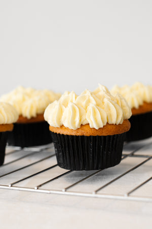 Several vanilla cupcakes with piped vanilla butter cream on a cooling rack