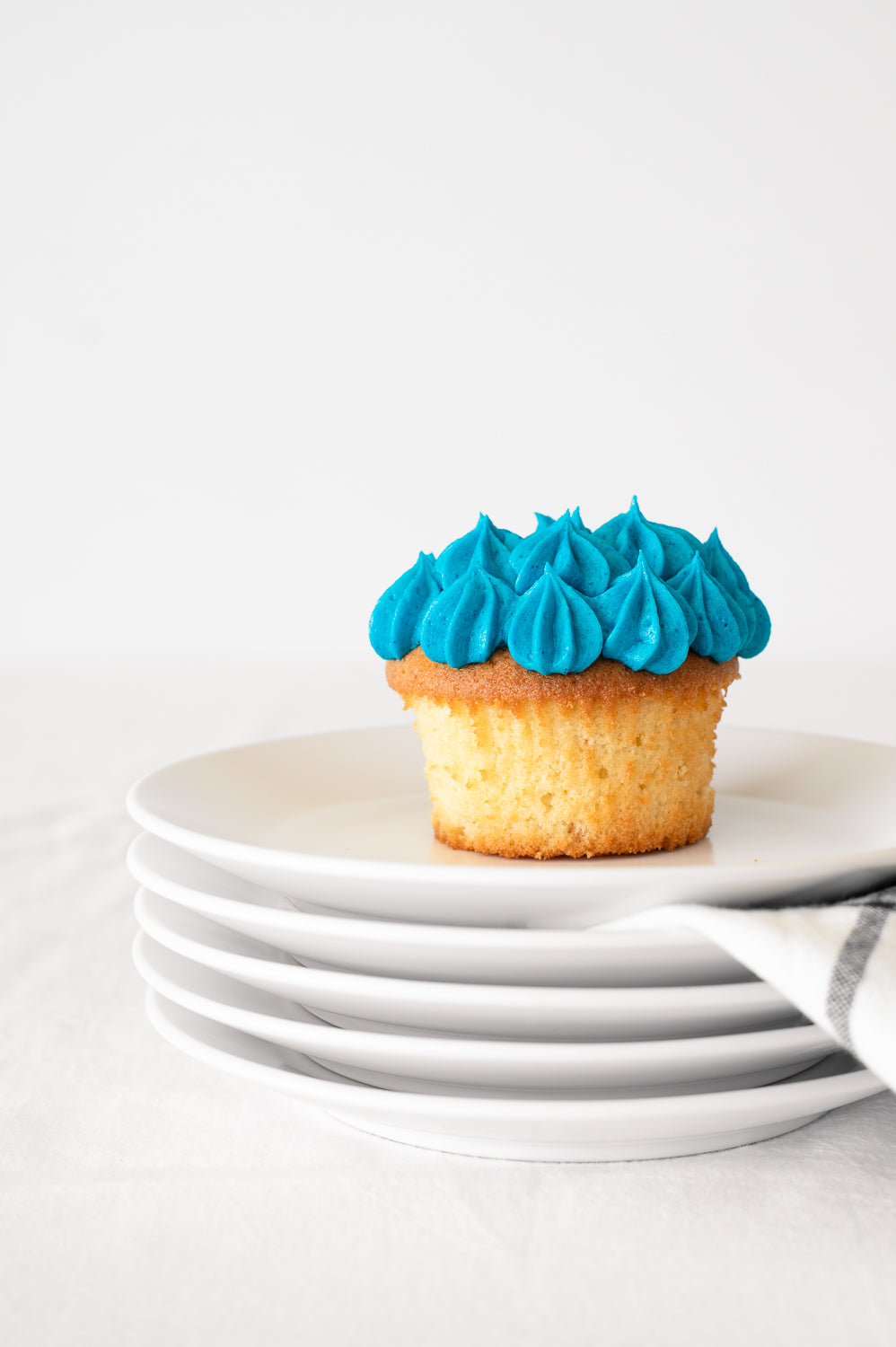 A stack of plates holding a vanilla cupcake with blue piped icing