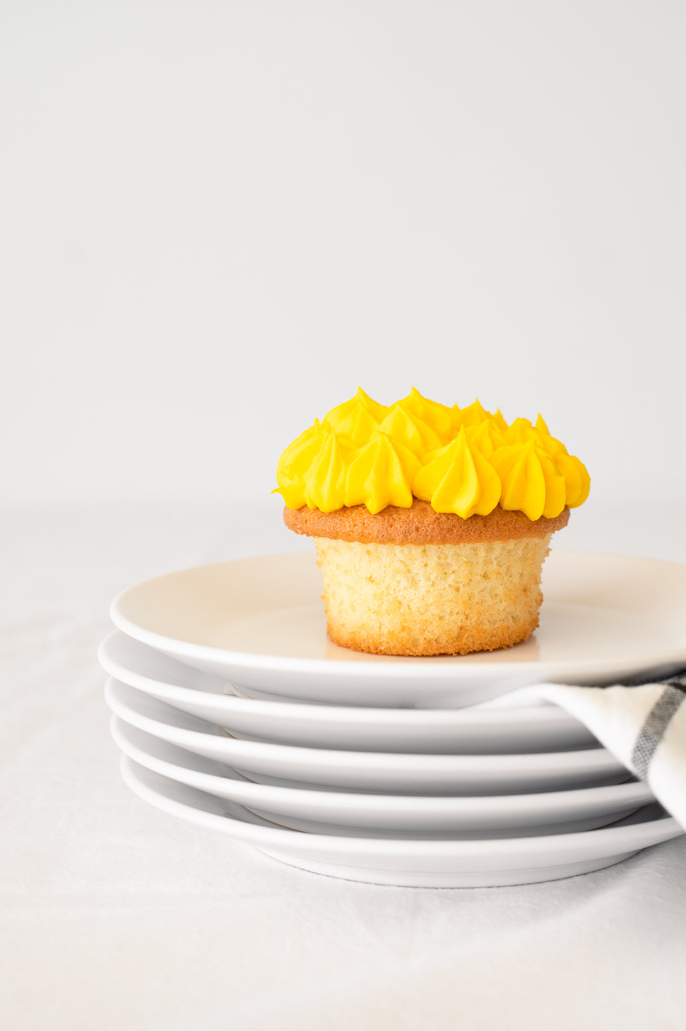 A stack of plates holding a vanilla cupcake with yellow piped icing