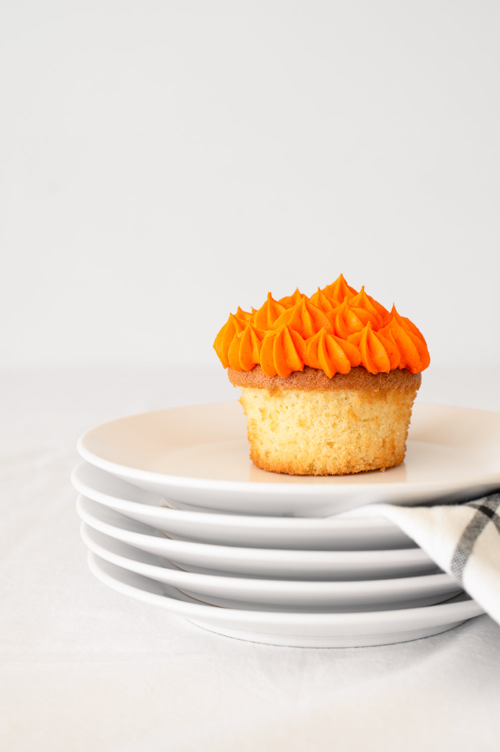 A stack of plates holding a vanilla cupcake with orange piped icing