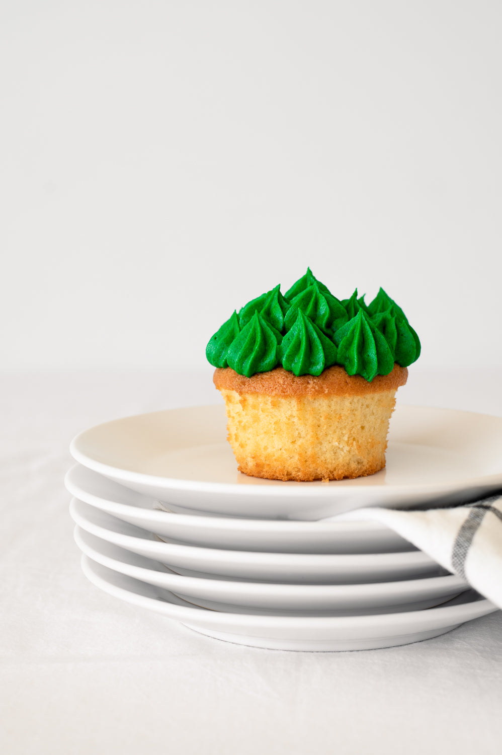 A stack of plates holding a vanilla cupcake with green piped icing