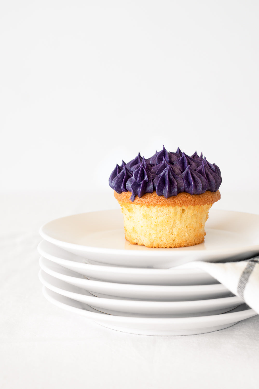 A stack of plates holding a vanilla cupcake with purple piped icing