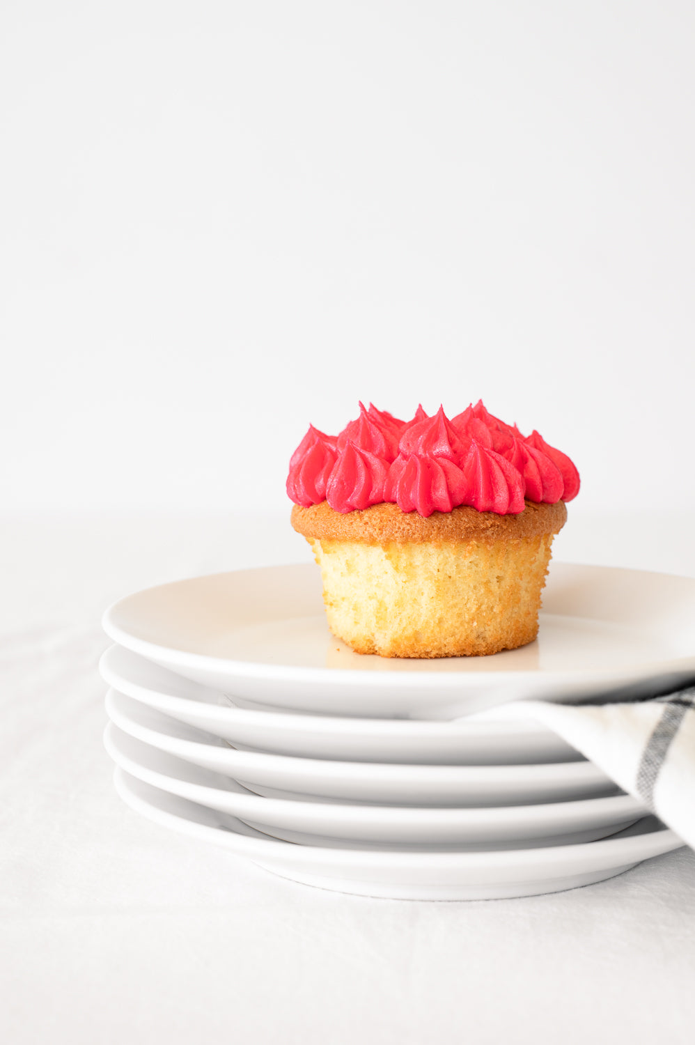 A stack of plates holding a vanilla cupcake with pink piped icing