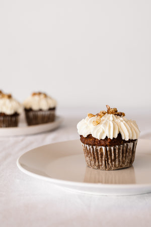 A single vegan carrot cake cup cake on a plate with piped whipped coconut cream on top