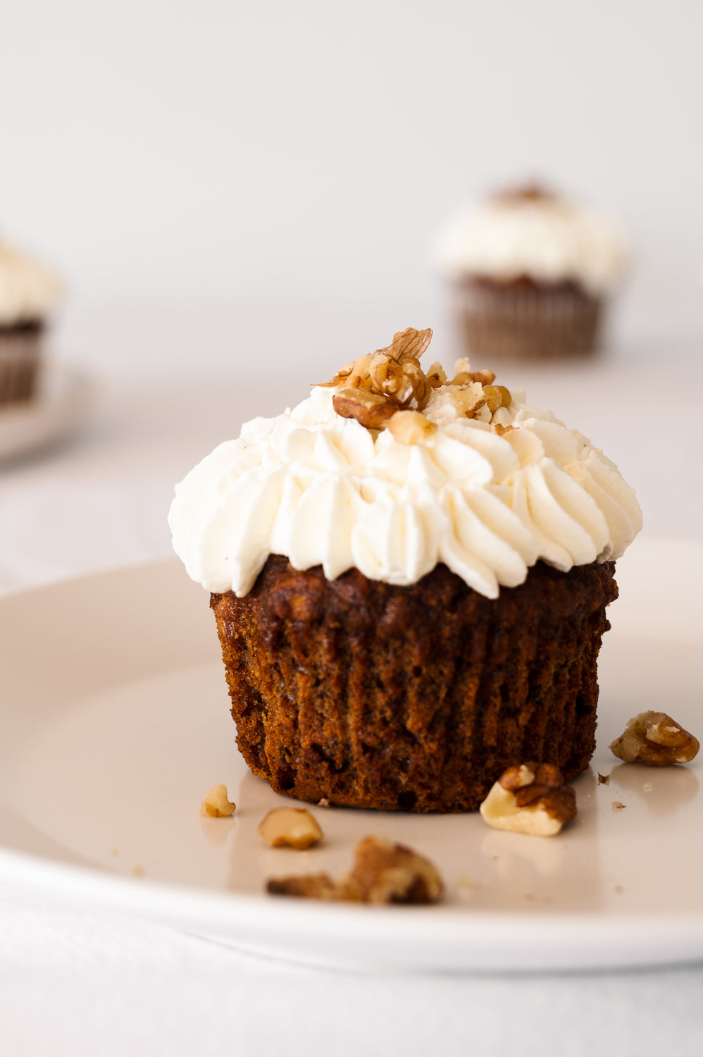 A single vegan carrot cake cup cake on a plate with piped whipped coconut cream on top
