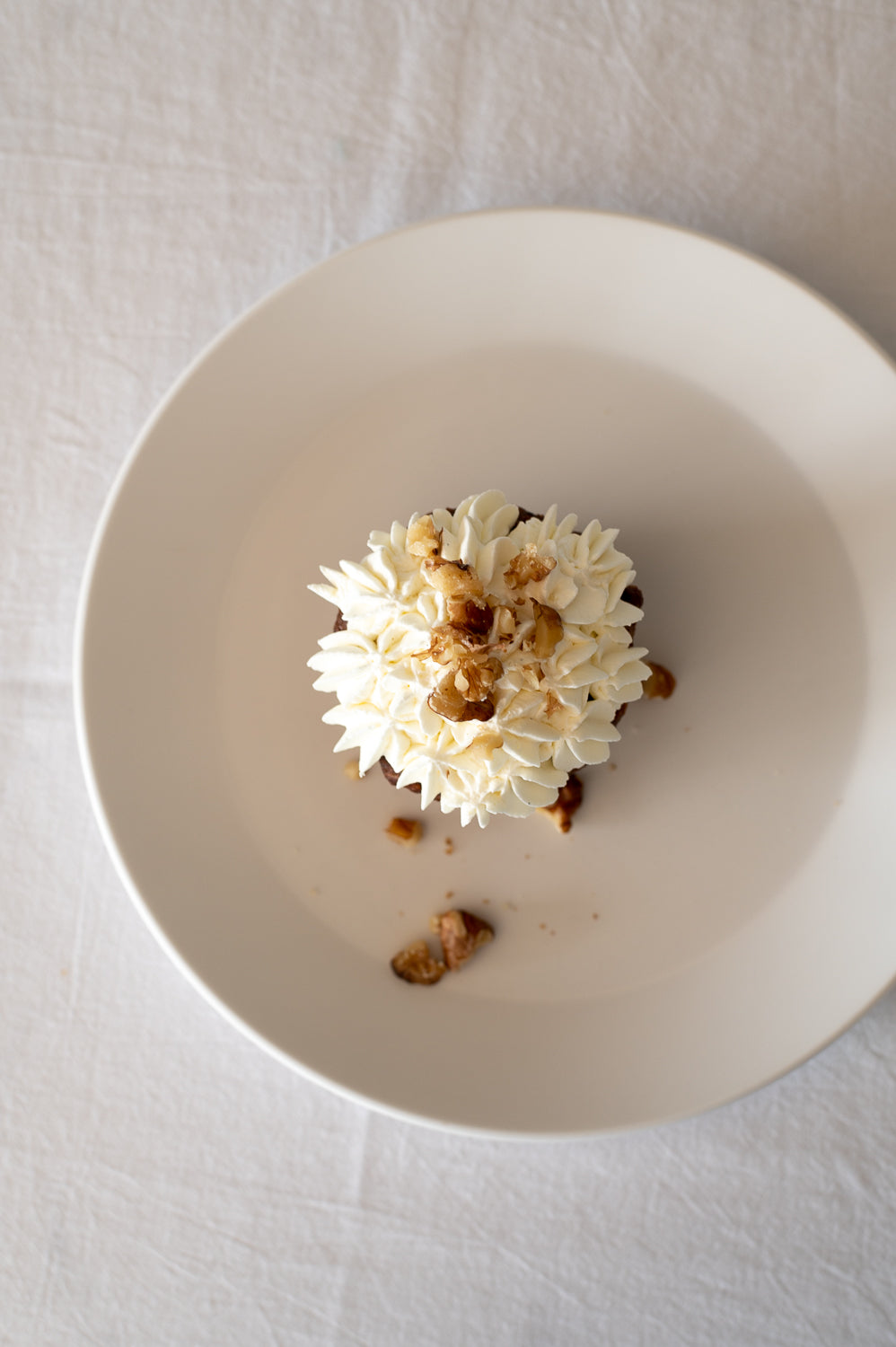 A top view of a vegan carrot cake cupcake on a plate with piped whipped coconut cream on top