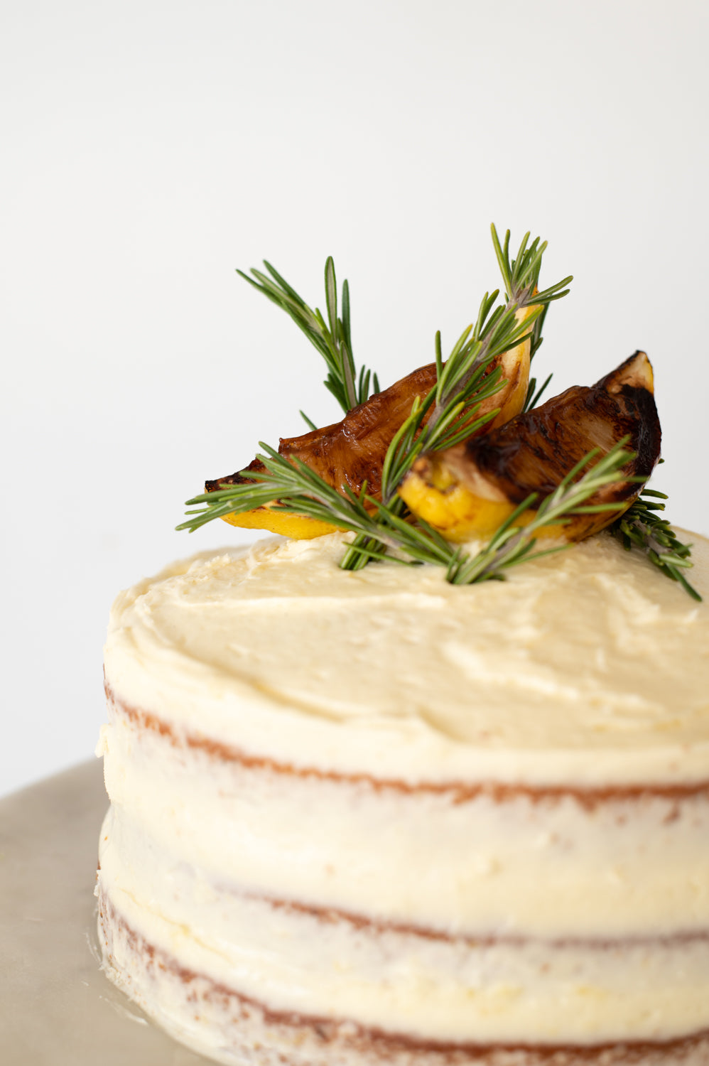 Three layered lemon, olive oil and rosemary cake covered in cream cheese icing, topped with lemon and rosemary garnish