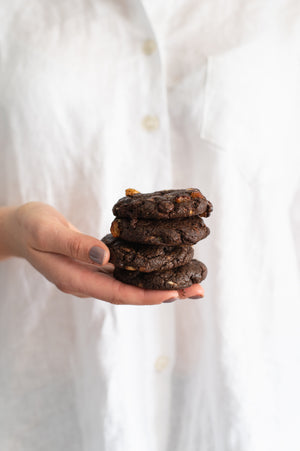 A hand holding a stack of chewy triple choc chip cookies