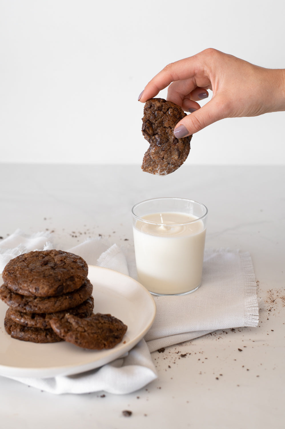 A hand holding a choc chip cookie, dunking it in milk