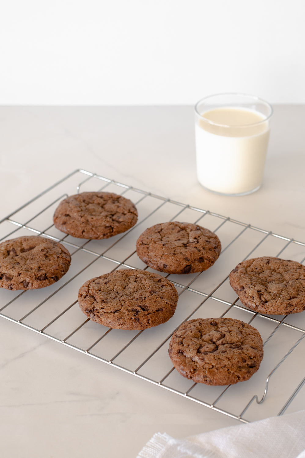 Choc chip cookies on a cooling rack with a glass of milk