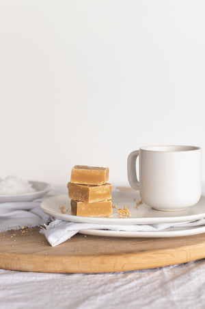 A stack of Salted Caramel Fudge on a wooden board with a mug