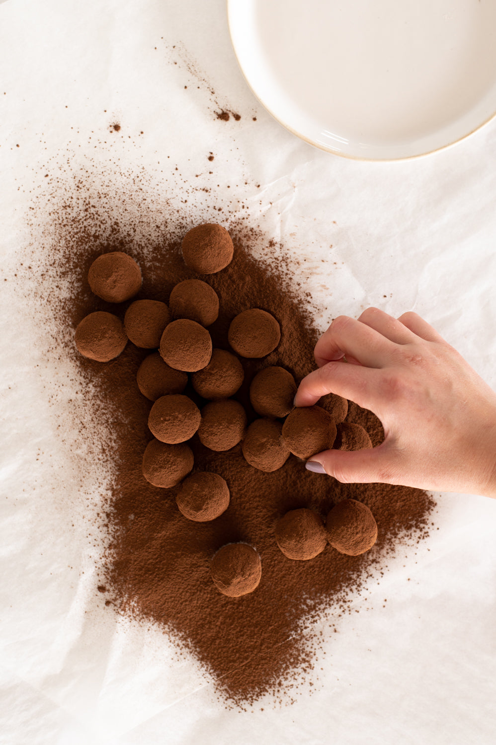 Someone taking a chocolate truffle from a pile of truffles on a table