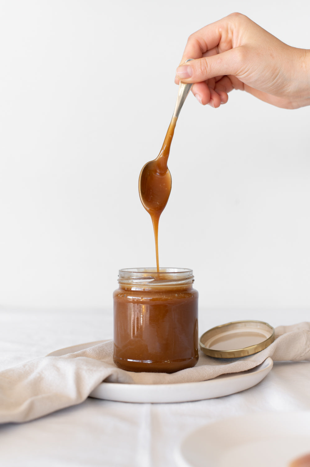 A spoon is lifted out of a jar with salted butter caramel 